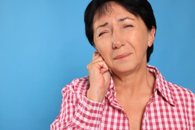 Photo of Senior woman suffering from ear pain on light blue background, closeup. Space for text
