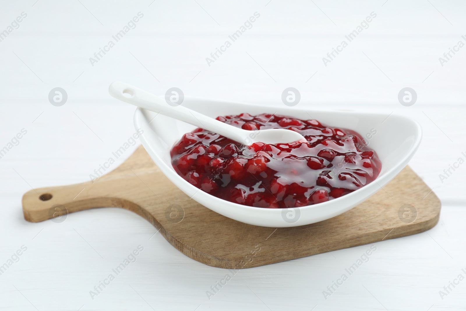 Photo of Fresh cranberry sauce in bowl and spoon on white wooden table, closeup