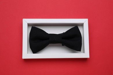 Stylish black bow tie on red background, top view