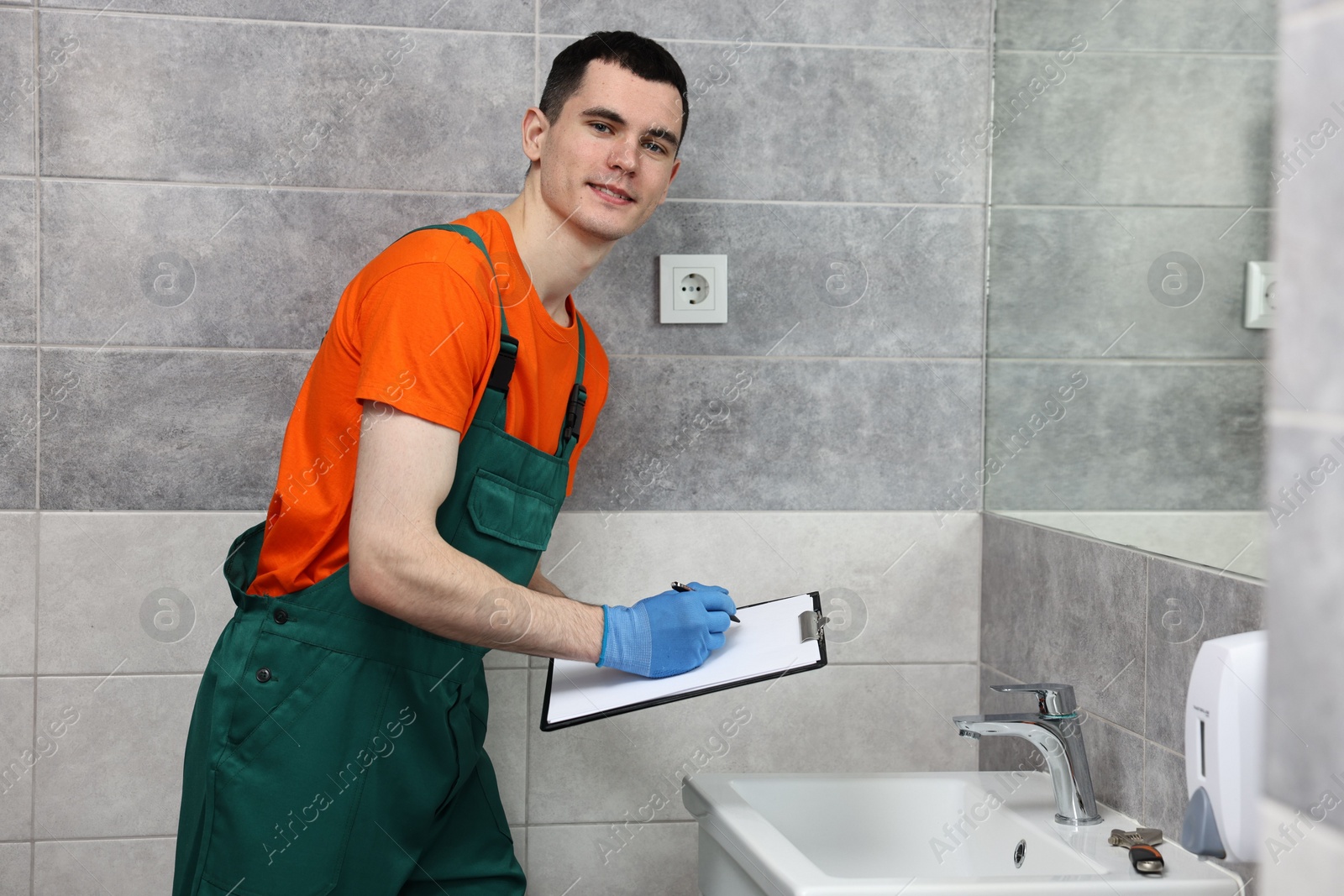 Photo of Young plumber writing results of examining sink in bathroom