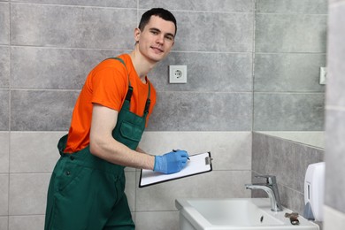 Photo of Young plumber writing results of examining sink in bathroom