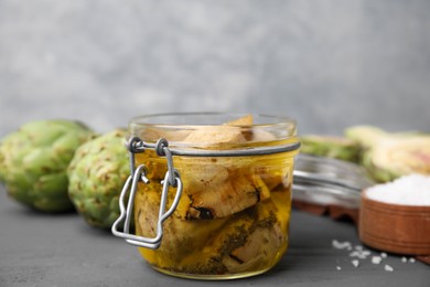 Photo of Jar of delicious artichokes pickled in olive oil on grey table, closeup