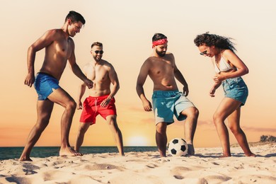 Image of Happy friends playing football on beach during sunset