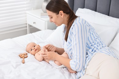 Photo of Young woman applying body cream onto baby`s skin on bed