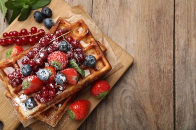 Photo of Board with delicious Belgian waffles, berries and powdered sugar on wooden table, top view. Space for text