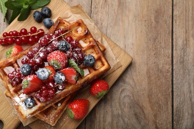 Board with delicious Belgian waffles, berries and powdered sugar on wooden table, top view. Space for text