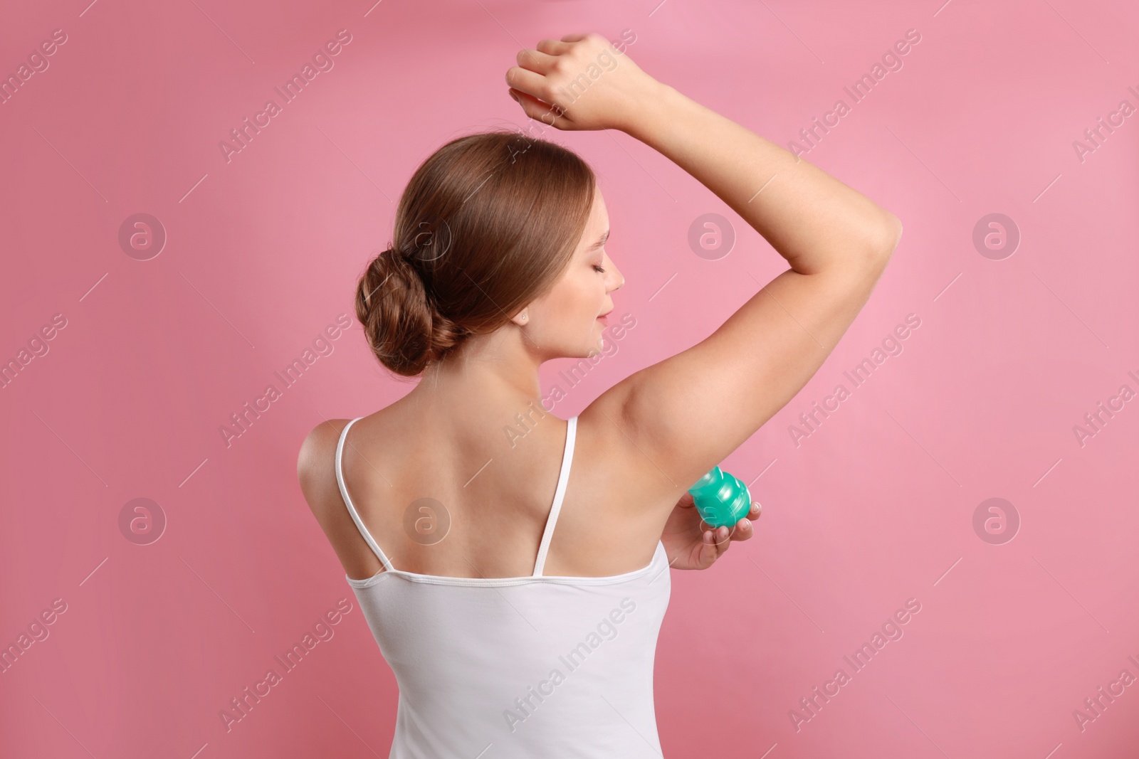 Photo of Young woman applying deodorant to armpit on pink background