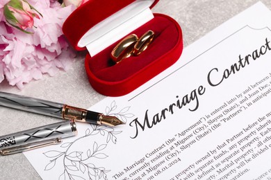 Marriage contract, fountain pen, golden wedding rings and flowers on grey table