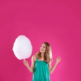 Happy young woman with cotton candy on pink background