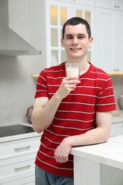 Photo of Happy man with milk mustache holding glass of tasty dairy drink in kitchen