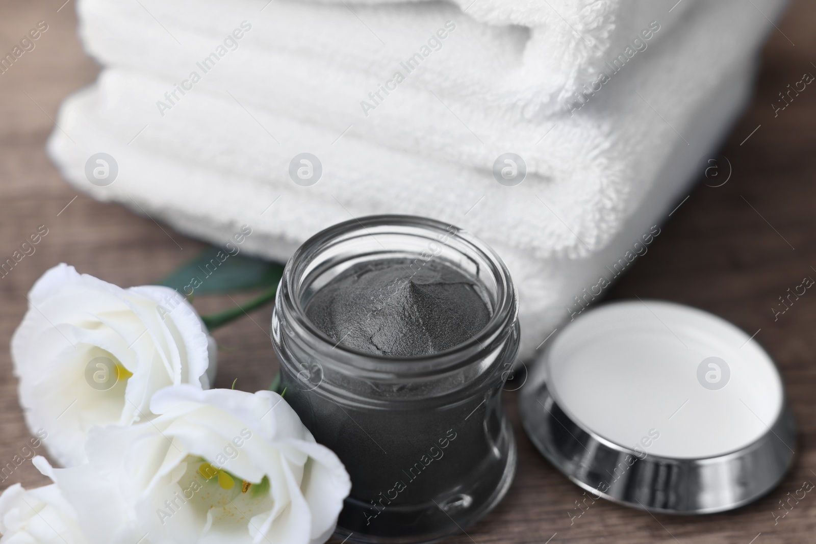 Photo of Folded towels, jar of cosmetic mask and eustoma flowers on wooden table