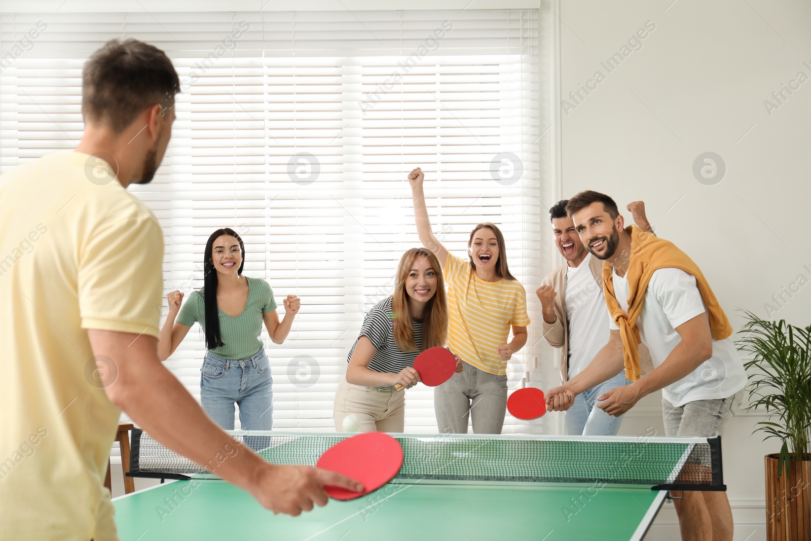 Photo of Happy friends playing ping pong together indoors