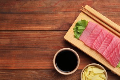 Photo of Tasty sashimi (pieces of fresh raw tuna), lettuce, soy sauce and ginger slices on wooden table, flat lay. Space for text