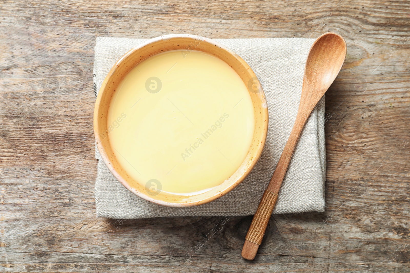 Photo of Bowl with condensed milk and spoon on wooden background, top view. Dairy products