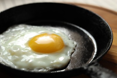 Photo of Frying pan with tasty cooked egg on wooden board, closeup
