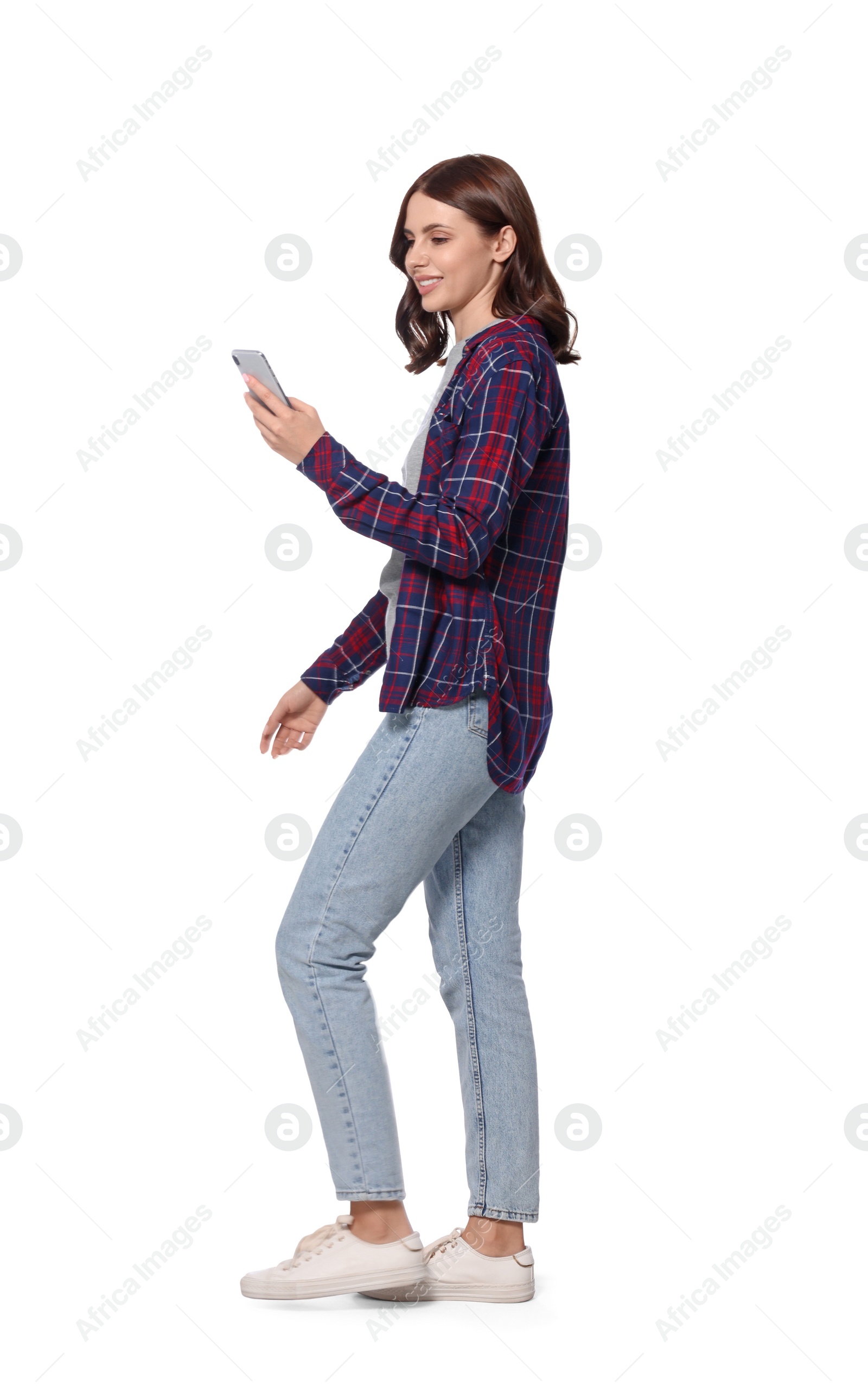 Photo of Happy young woman in casual outfit using smartphone while walking on white background