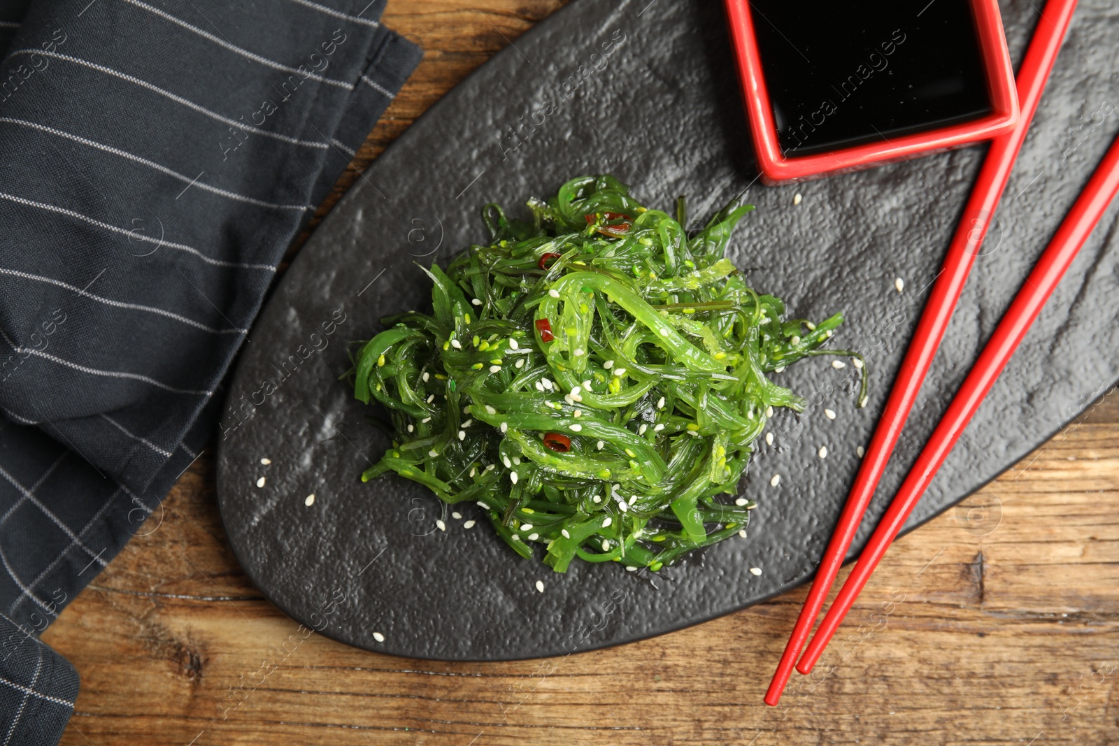 Photo of Japanese seaweed salad served on wooden table, flat lay