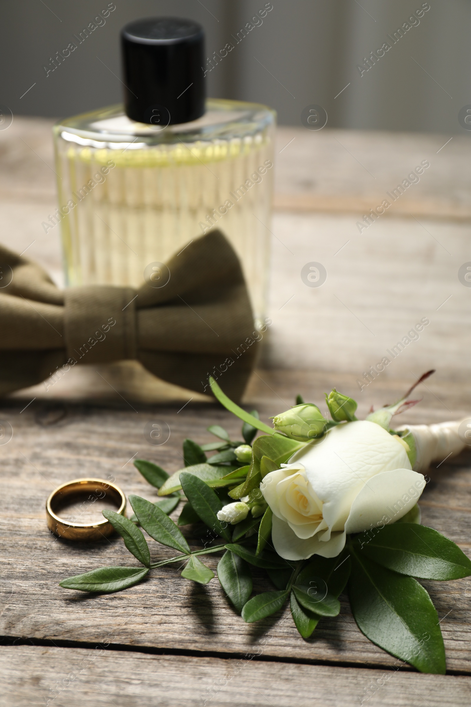 Photo of Wedding stuff. Stylish boutonniere, perfume, bow tie and ring on wooden table, closeup