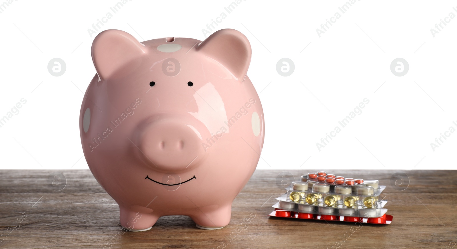 Photo of Piggy bank and pills on wooden table against white background. Medical insurance