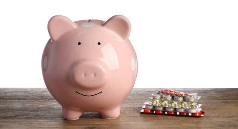 Piggy bank and pills on wooden table against white background. Medical insurance