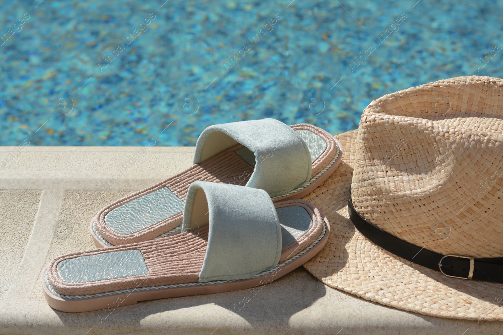 Photo of Stylish slippers and straw hat at poolside on sunny day. Beach accessories