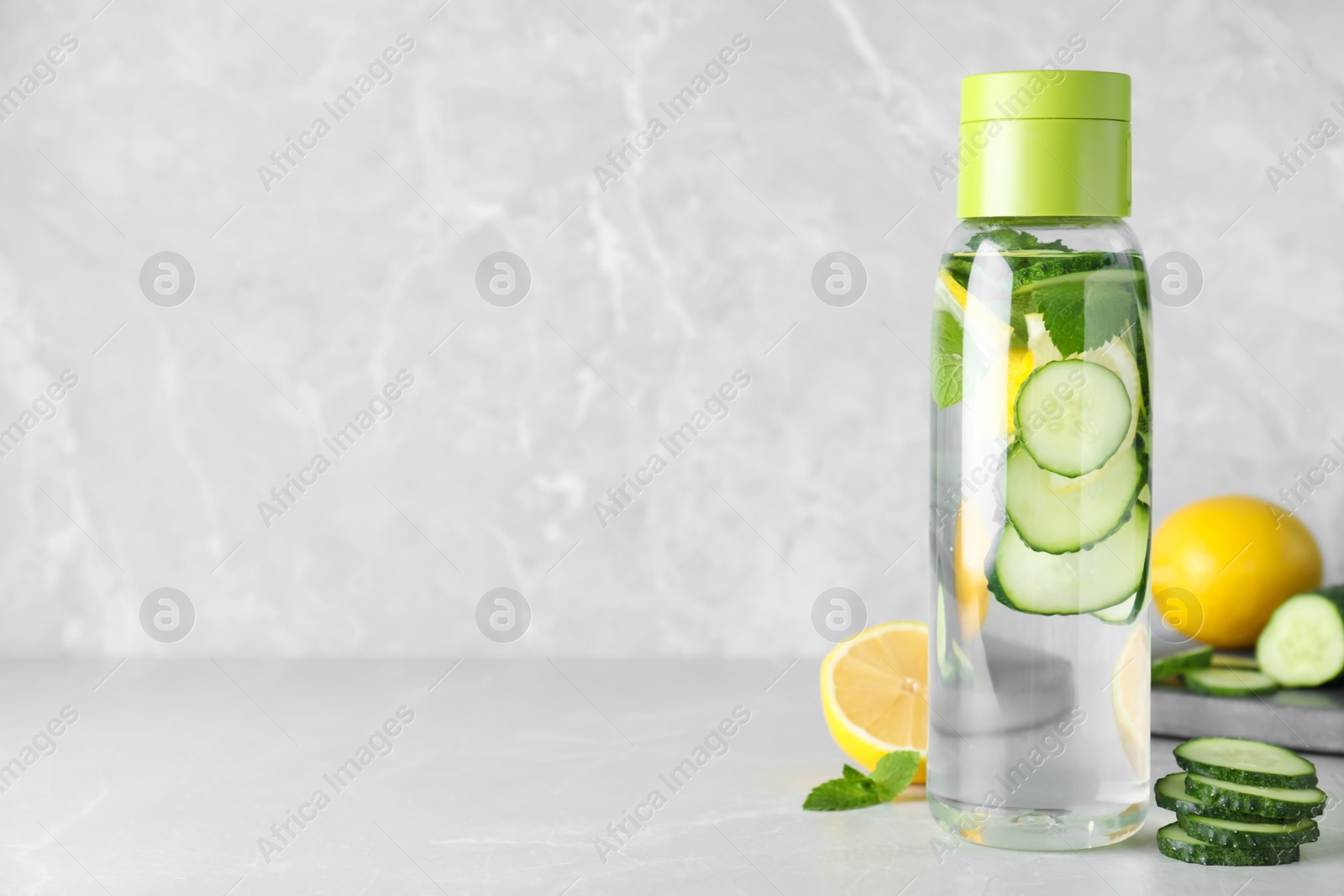 Photo of Bottle of refreshing water with cucumber, lemon and mint on light grey table, space for text