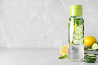Bottle of refreshing water with cucumber, lemon and mint on light grey table, space for text