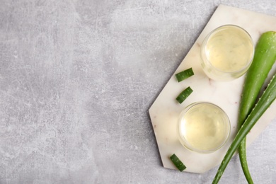 Photo of Fresh aloe drink in glasses and leaves on light grey table, flat lay. Space for text