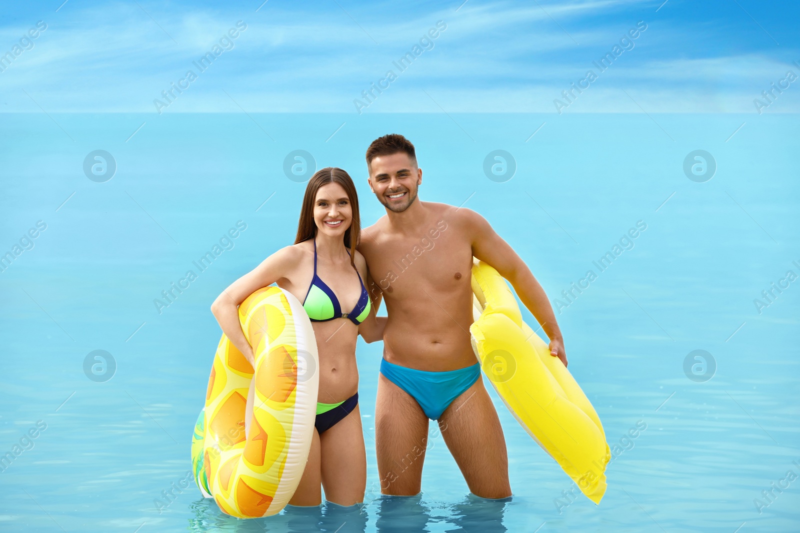 Photo of Young woman in bikini and her boyfriend with inflatable toys on beach. Lovely couple