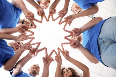 Photo of Team of volunteers putting their hands together on light background, bottom view