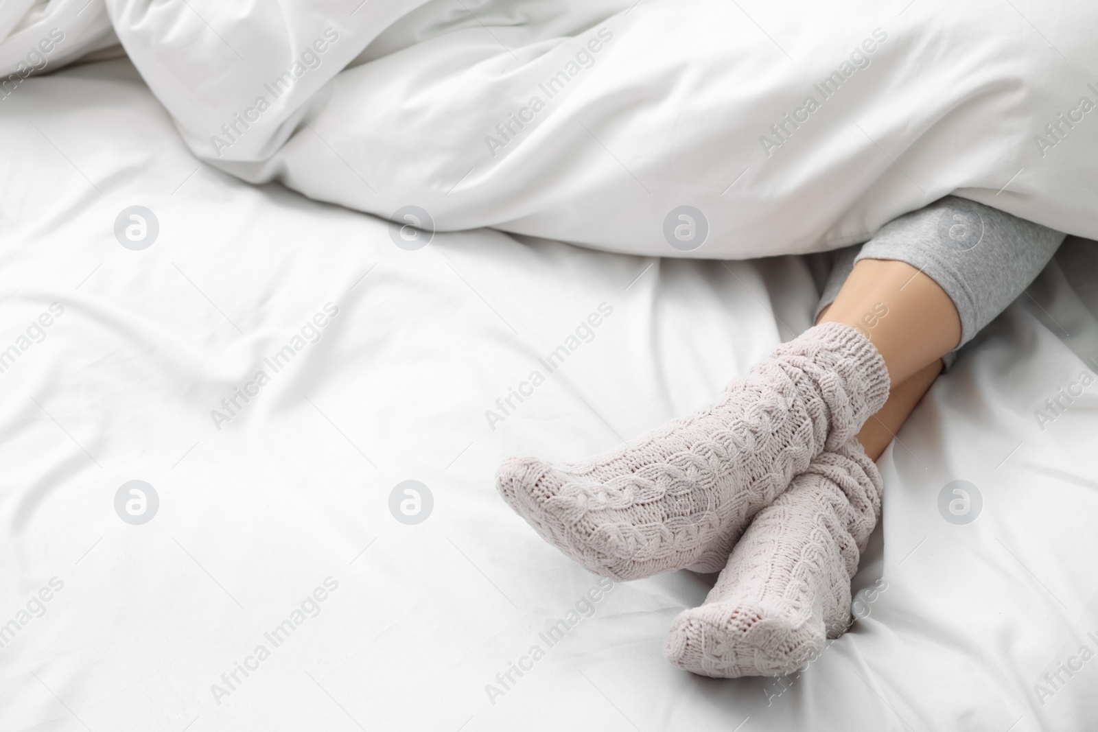 Photo of Woman wearing warm socks in comfortable bed, closeup. Space for text