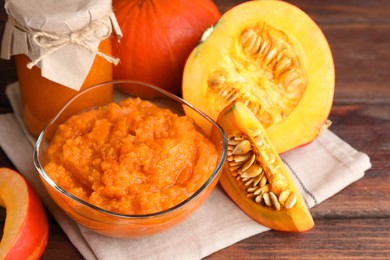 Photo of Bowl of pumpkin jam and fresh pumpkin on wooden table