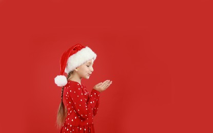 Image of Happy little child in Santa hat on red background, space for text. Christmas celebration