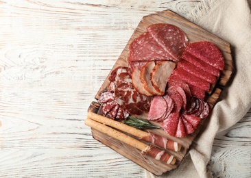 Photo of Cutting board with different sliced meat products on wooden background, flat lay. Space for text