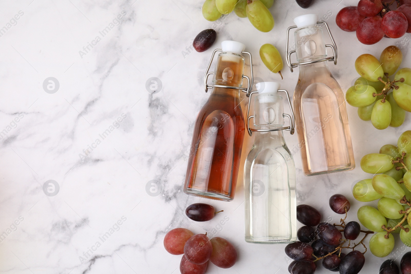 Photo of Different types of vinegar in bottles and grapes on light marble table, flat lay. Space for text