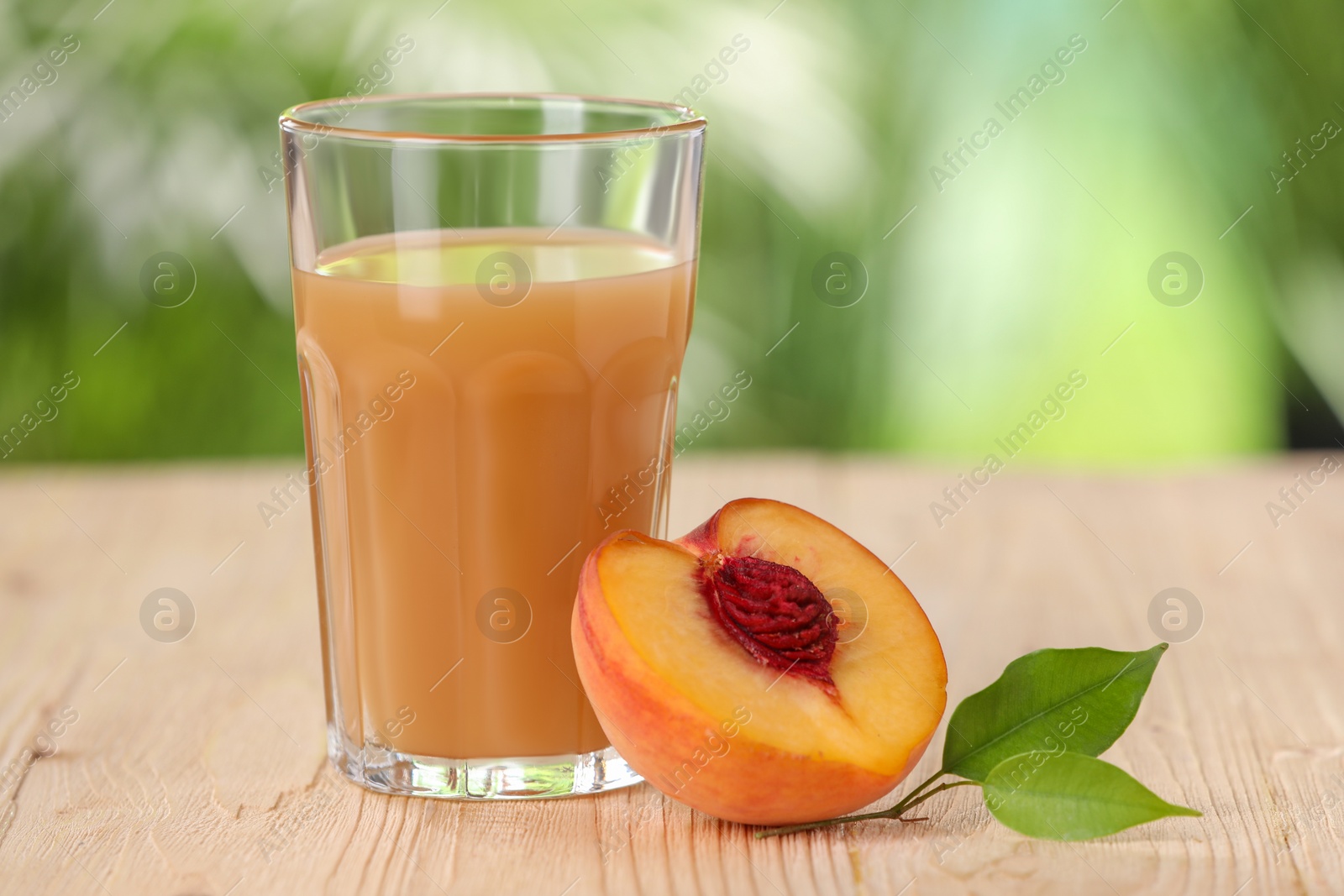 Photo of Tasty peach juice, fresh fruit and green leaves on wooden table outdoors, closeup