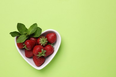 Photo of Fresh ripe strawberries with mint in heart shaped bowl on light green background, top view. Space for text