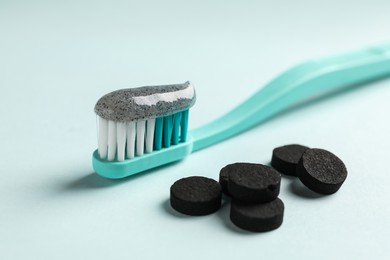 Photo of Brush with charcoal toothpaste and tablets on light background, closeup