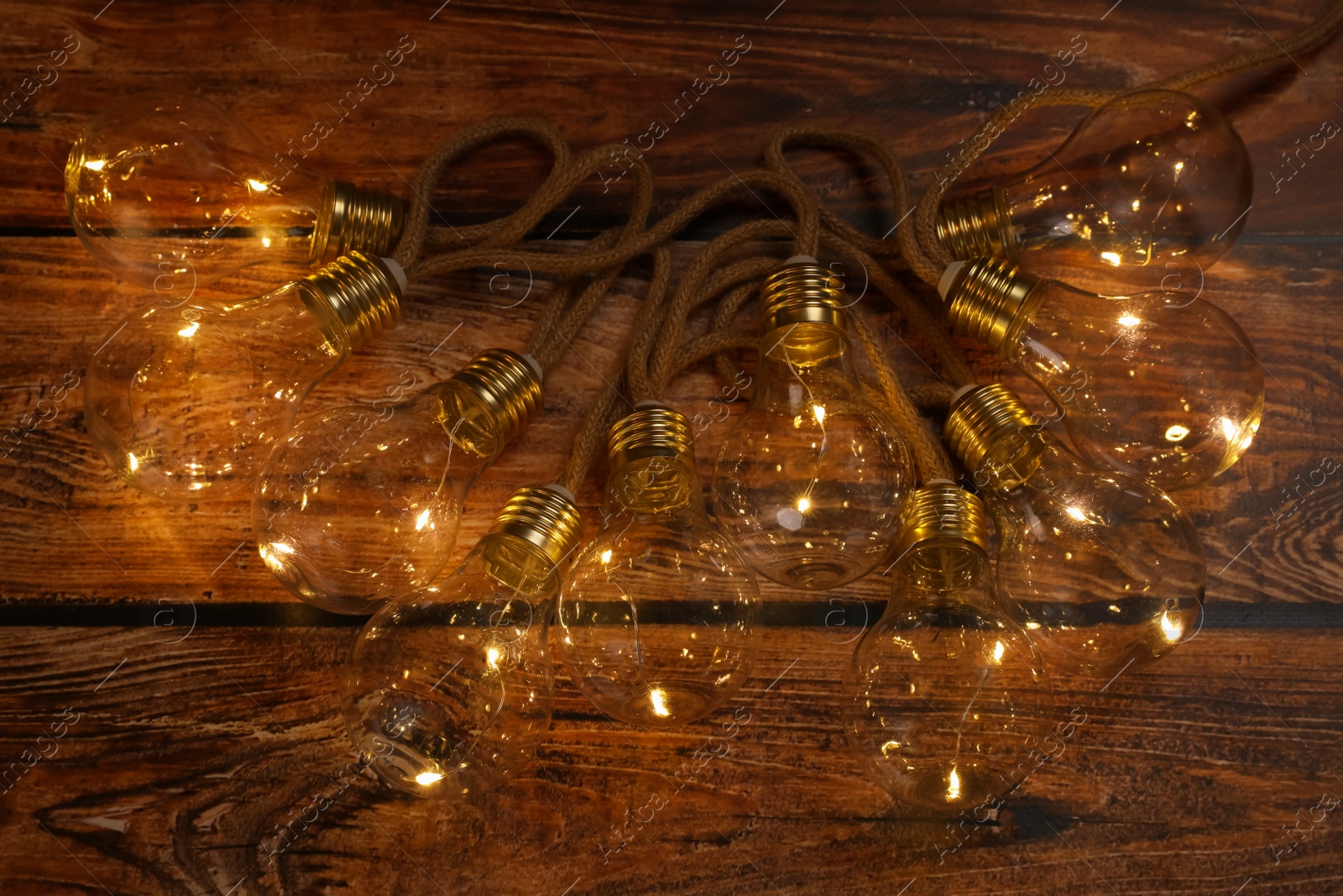 Photo of String lights with lamp bulbs on wooden table, top view