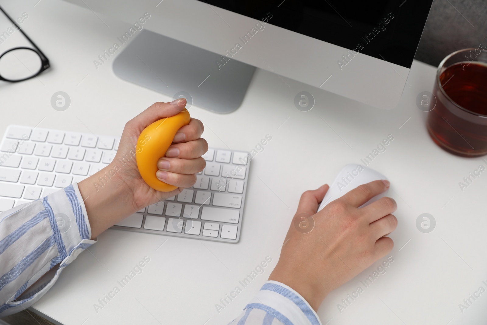 Photo of Woman squeezing antistress ball while working on computer in office, closeup
