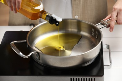 Photo of Vegetable fats. Woman pouring cooking oil into frying pan on stove, closeup