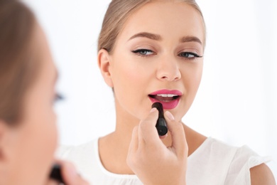 Photo of Beautiful young woman applying lipstick in front of mirror