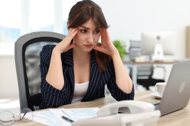 Photo of Overwhelmed office worker sitting at table with laptop and documents indoors