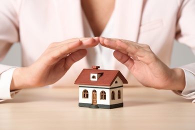 Female agent covering house model at table, closeup. Home insurance