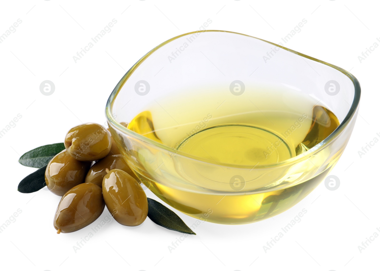 Photo of Glass bowl of oil, ripe olives and green leaves on white background