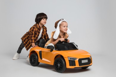 Photo of Cute boy pushing children's electric toy car with little girl on grey background