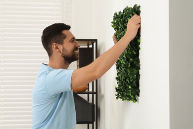 Man installing green artificial plant panel on white wall in room