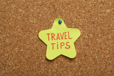 Photo of Colorful paper note with phrase Travel Tips pinned to cork board, closeup