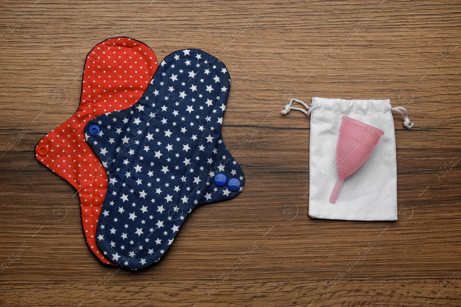 Photo of Reusable cloth pads and menstrual cup on wooden table, flat lay