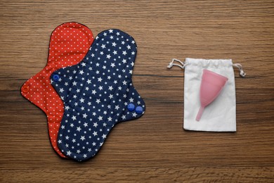 Reusable cloth pads and menstrual cup on wooden table, flat lay